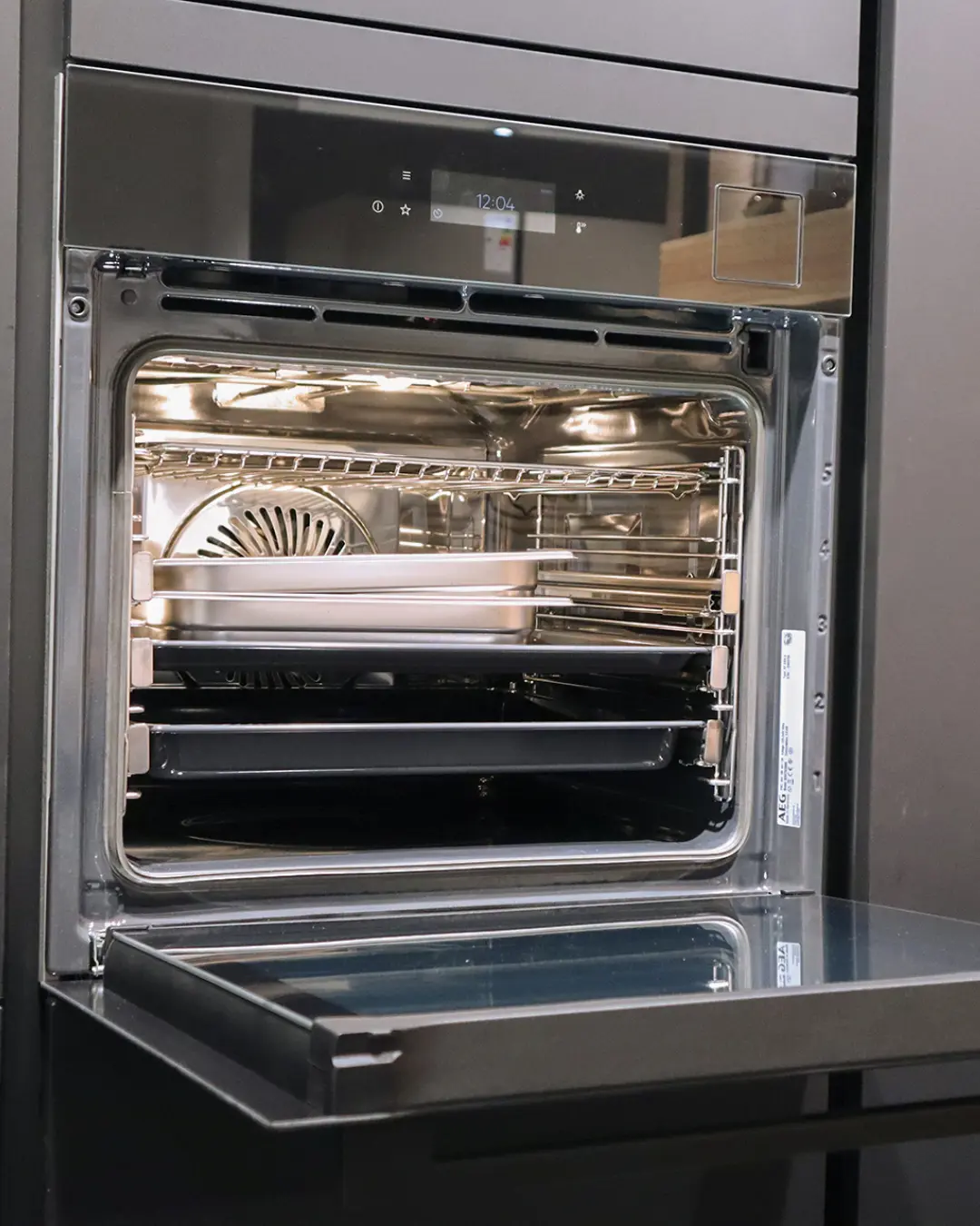 Geöffneter Einbaubackofen mit Touch-Display und Blechen in der grifflosen graphitschwarzen Nobilia Küche MGH12