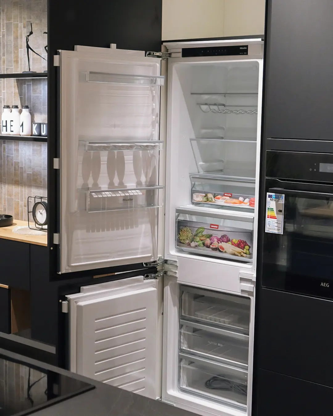 Geöffneter Miele Einbaukühlschrank in graphitschwarzer grifflosen Nobilia Küche MGH12, daneben AEG Backofen