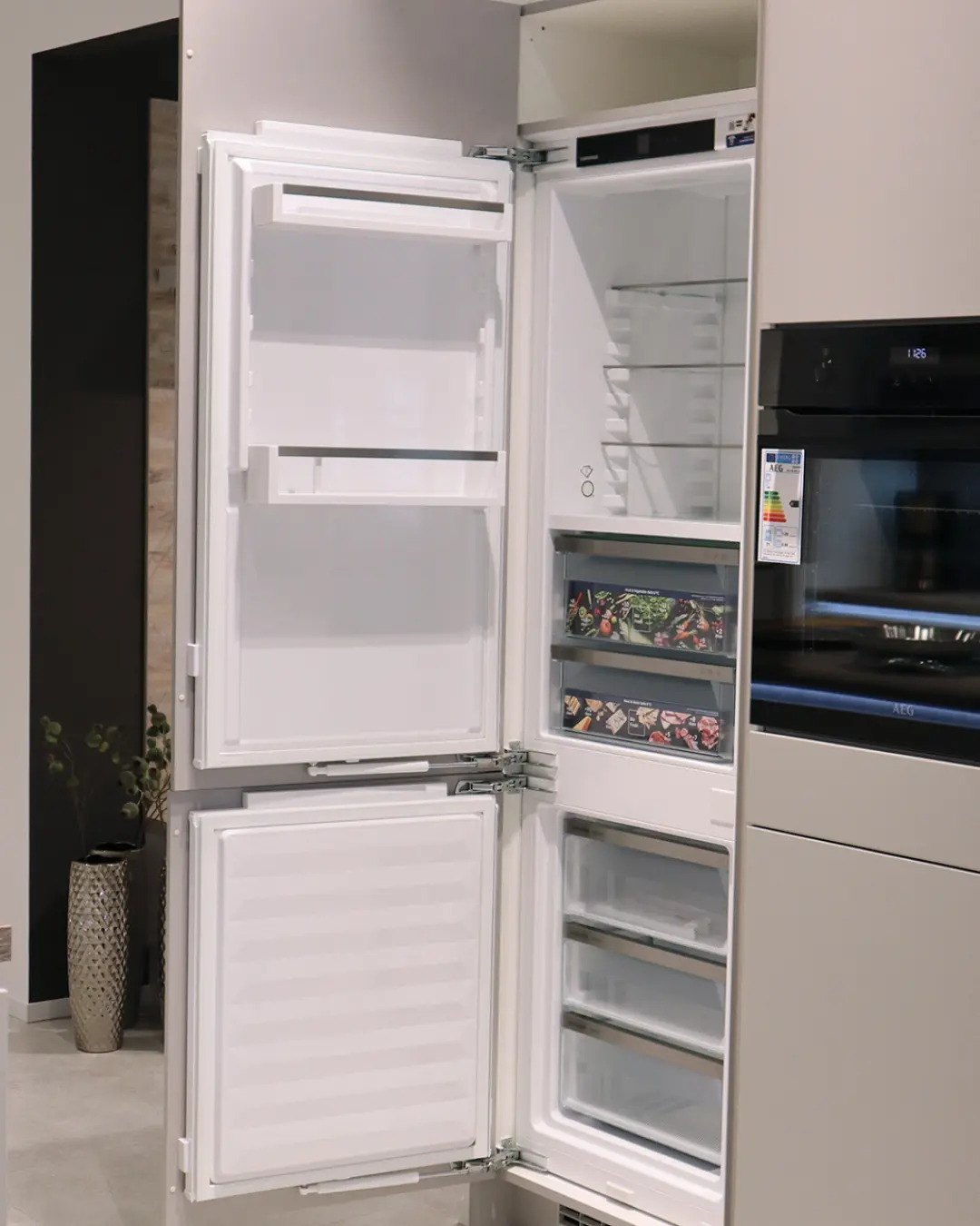 Geöffneter Einbaukühlschrank im Hochschrank der grifflosen grauen Nobilia Küche, daneben AEG Backofen