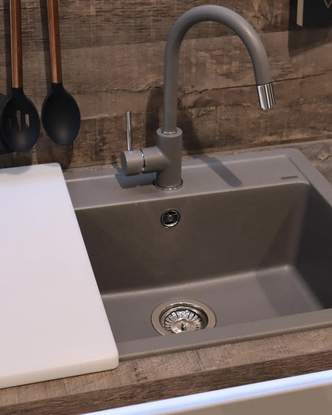 Detail der grauen grifflosen Nobilia Küche MGH9: graue Einbauspüle mit passender Armatur und Schneidbrett vor Holzoptik-Wand