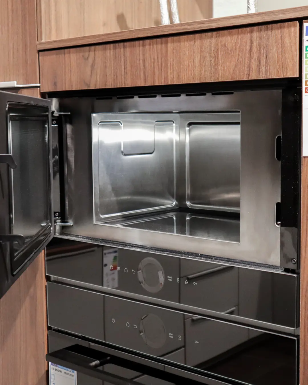 Hochschrank mit geöffnetem Mikrowellengerät und Backofen in der Nobilia-Küche in G-Form, Front in Holzoptik