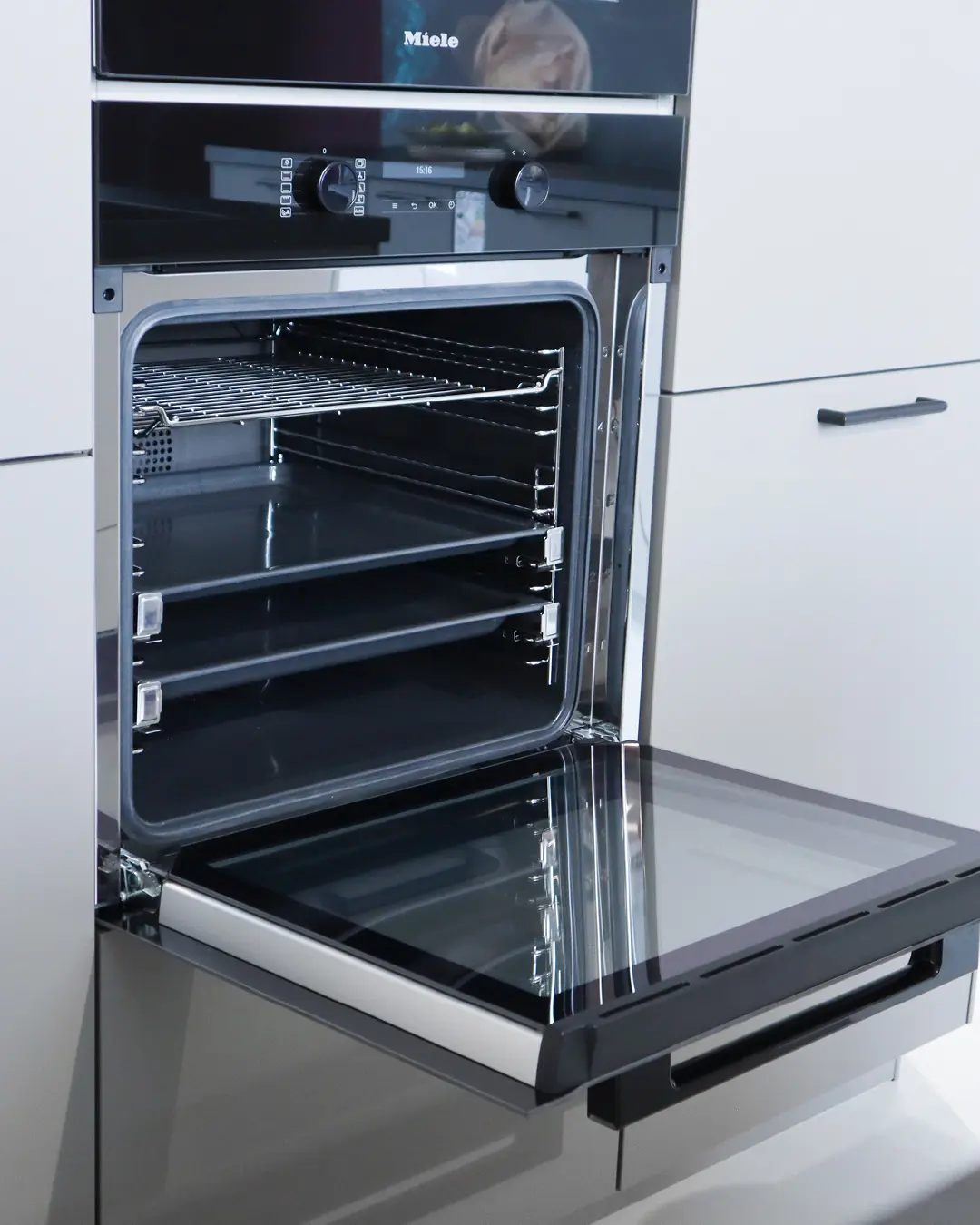 Geöffneter Miele-Einbaubackofen mit Einschubrosten in weißer Hochschrankfront der Nobilia Küche KFB12