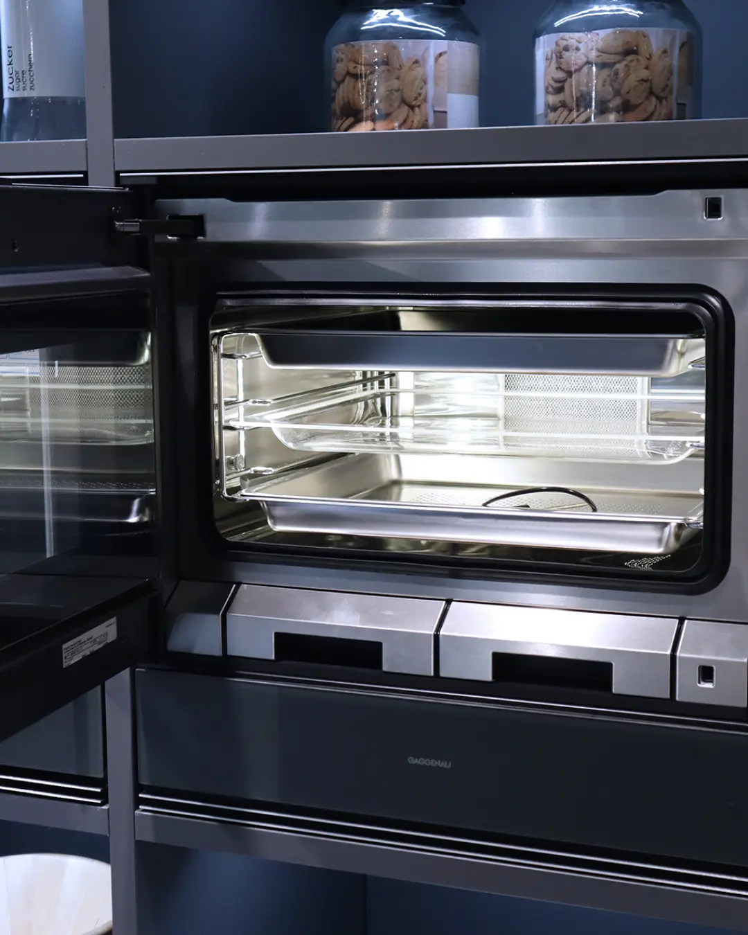 Geöffneter Gaggenau-Dampfbackofen mit beleuchtetem Garraum im Hochschrank der carbongrauen Leicht Küche KBK23