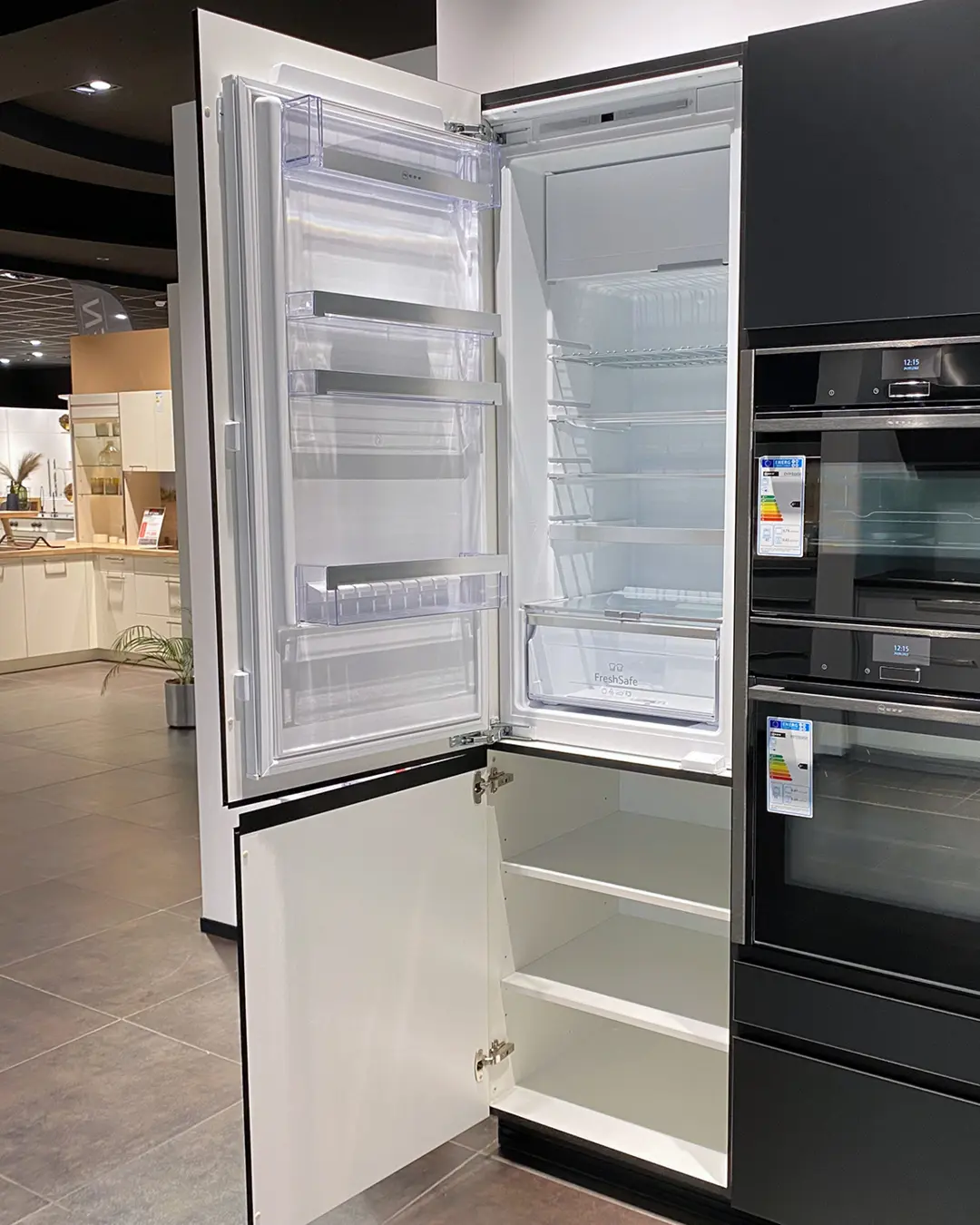 Geöffneter Einbaukühlschrank in der matt-weißen Nobilia Küche KSD13, daneben schwarze Einbaugeräte im Hochschrank
