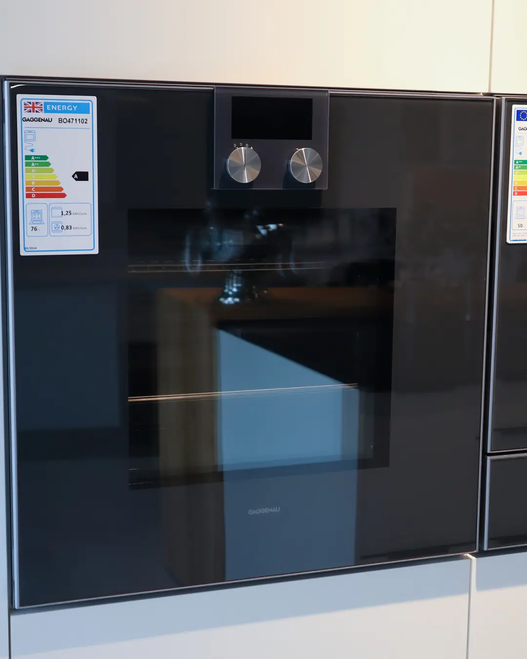 Eingebauter schwarzer Gaggenau-Backofen mit Drehreglern in der weißen Häcker Küche KBK17