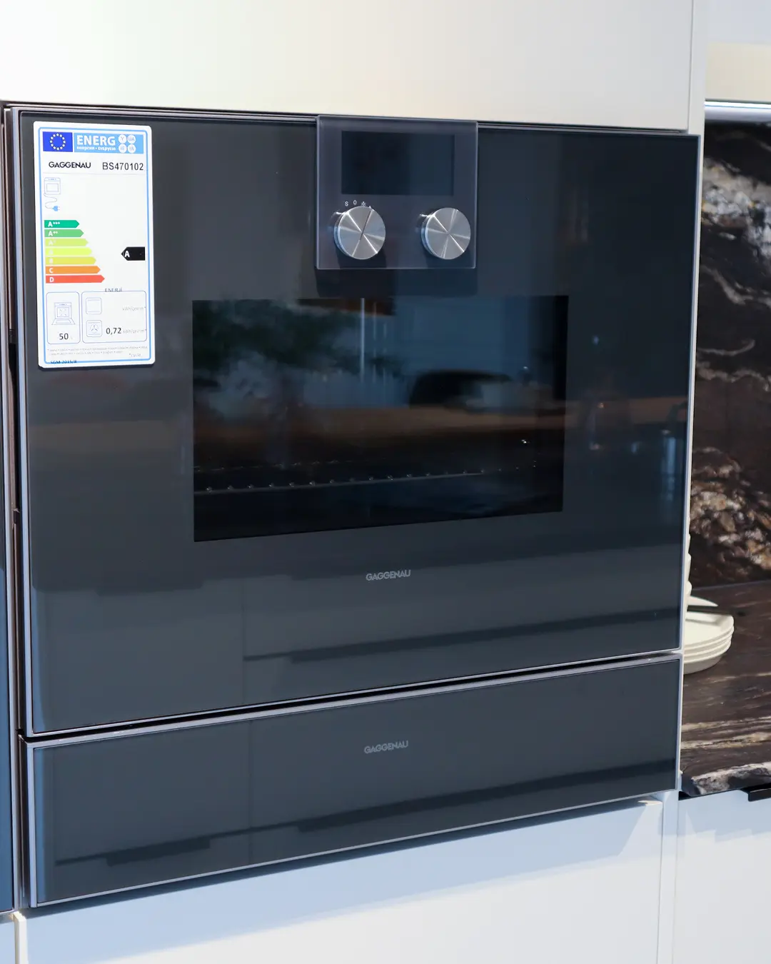 Eingebauter Gaggenau Dampfbackofen mit Wärmeschublade in weißer Häcker Küche, daneben Wandpaneel in Steinoptik
