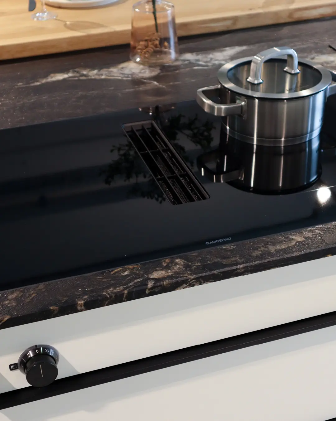 Kochinsel der weißen Häcker Küche KBK17 mit Gaggenau-Induktionsfeld, Muldenlüfter und Topf, Arbeitsplatte in Steinoptik