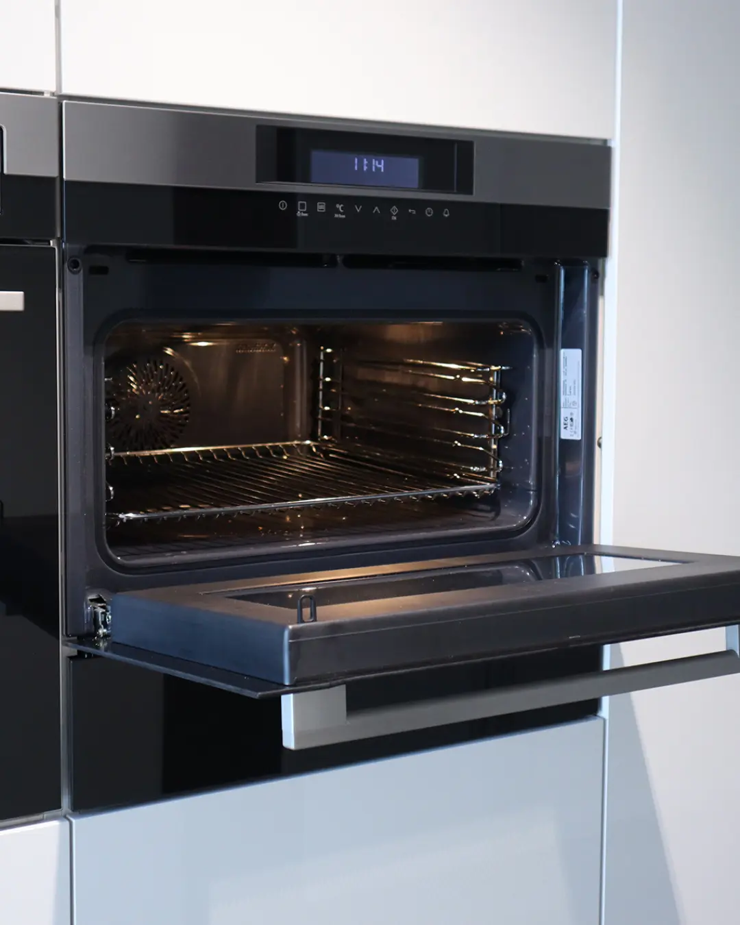 Geöffneter Einbaubackofen in dunklem Design in der Hochschrankzeile der weißen Leicht Küche KCR1