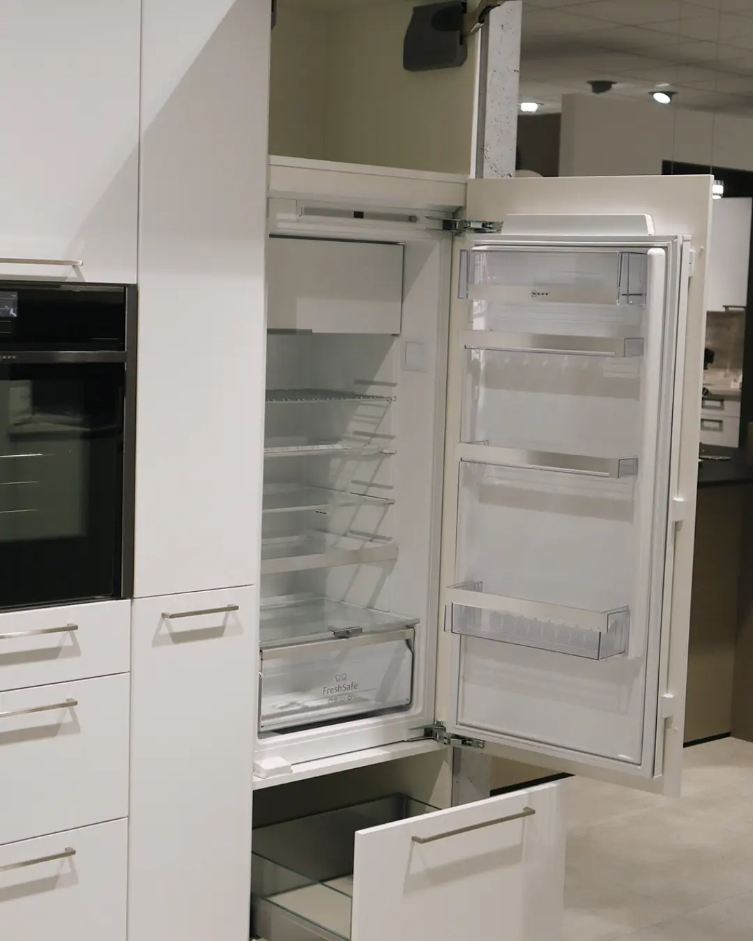 Geöffneter Einbaukühlschrank im Hochschrank der weißen Nobilia Küche in L-Form, daneben Einbaubackofen