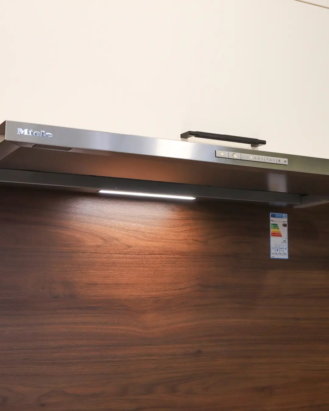 Flachschirmhaube von Miele mit LED-Licht über Rückwand in Holzoptik in weißer Nobilia Küche in U-Form