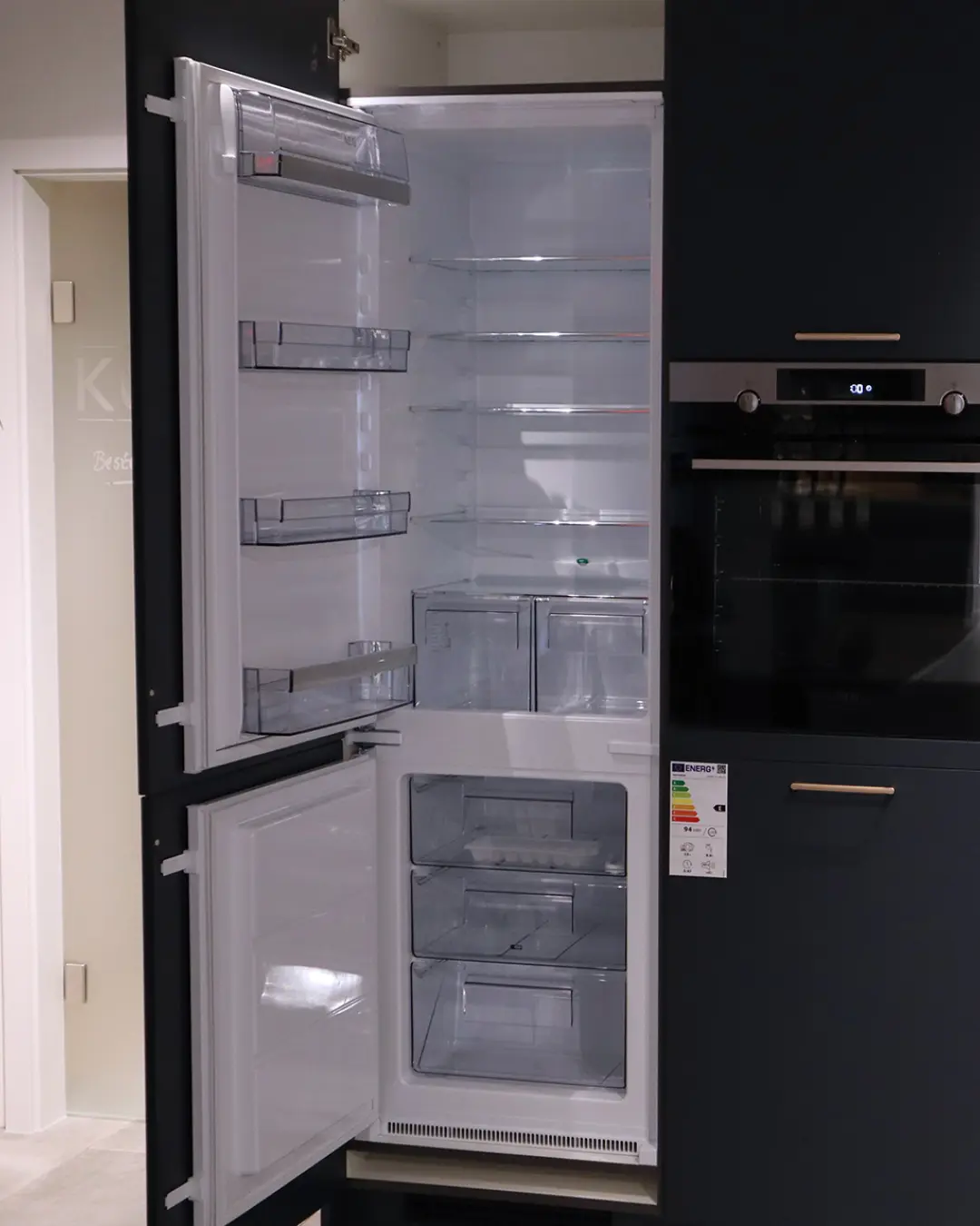 Geöffneter Einbaukühlschrank mit Gefrierfach in der fjordblauen Nobilia Küche, daneben Einbaubackofen
