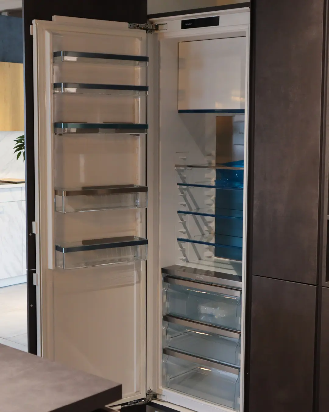 Geöffneter Einbaukühlschrank mit leeren Glasablagen in der grifflosen grauen Häcker Küche in U-Form