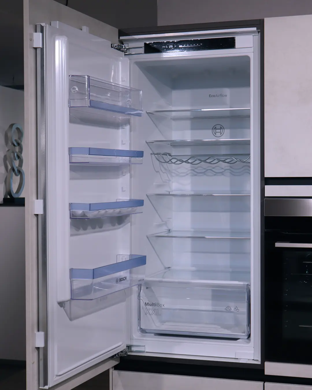 Geöffneter Einbaukühlschrank von Bosch mit leeren Glasablagen und MultiBox in der grifflosen U-Küche von Nobilia