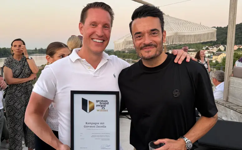 Zwei Männer bei einer Abendveranstaltung mit Urkunde "German Brand Award 25 Winner – Kampagne mit Giovanni Zarrella"