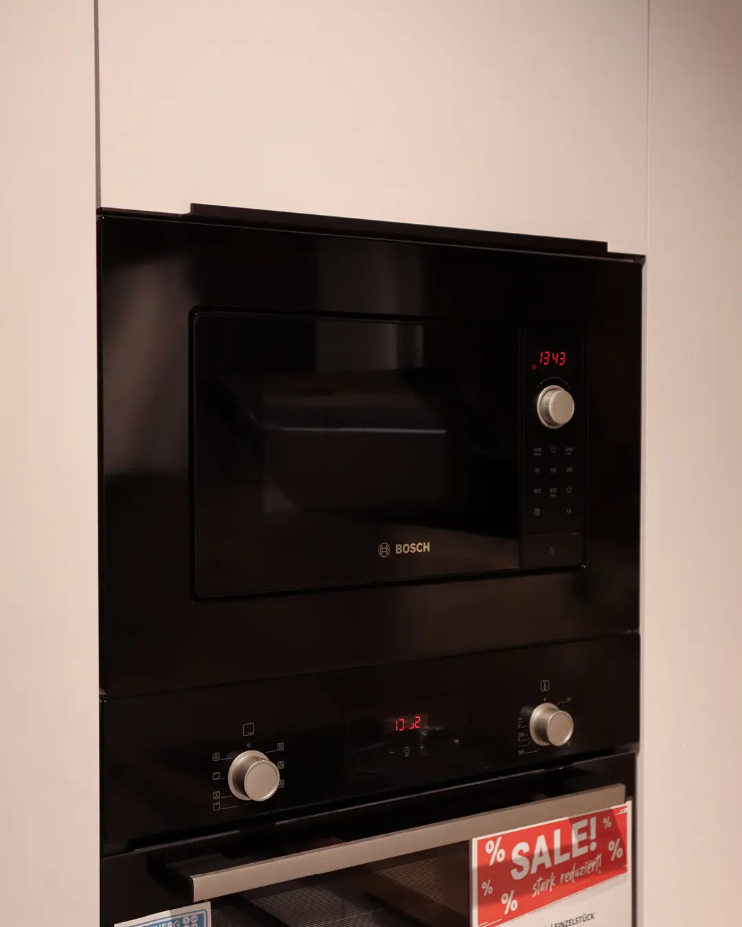 Eingebaute Bosch Mikrowelle und Backofen in weißer Häcker Küche mit Schild "SALE! stark reduziert"
