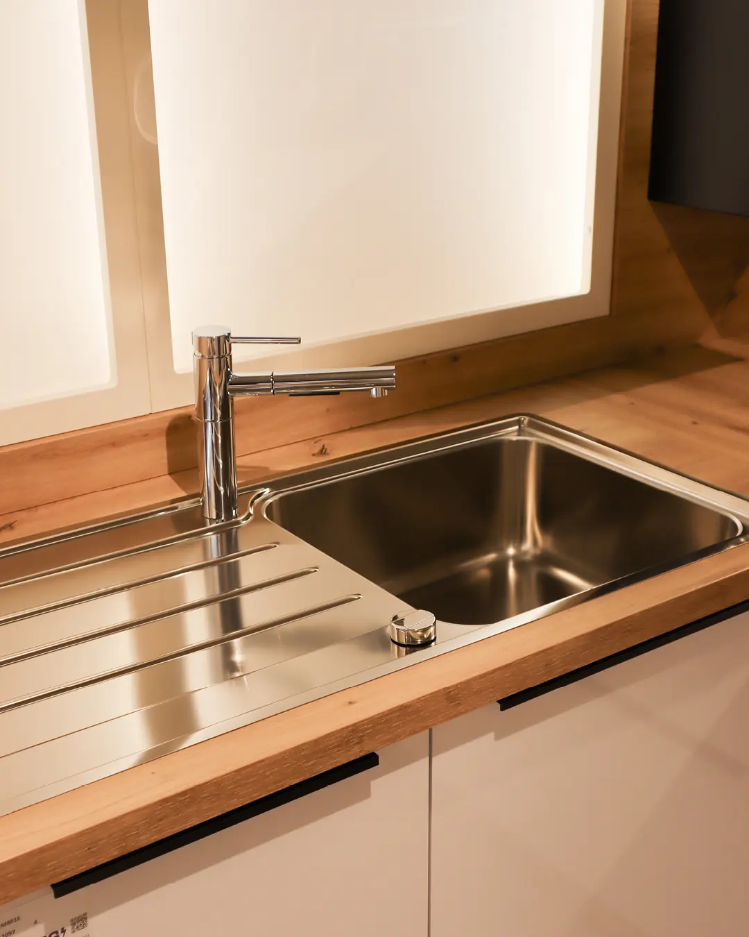 Edelstahlspüle mit Abtropffläche und Chromarmatur auf Arbeitsplatte in Holzoptik der weißen Häcker Küche KBK7