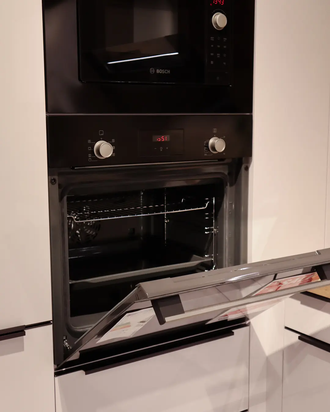 Geöffneter Einbaubackofen mit Bosch-Mikrowelle darüber in weißer Häcker Küche in G-Form