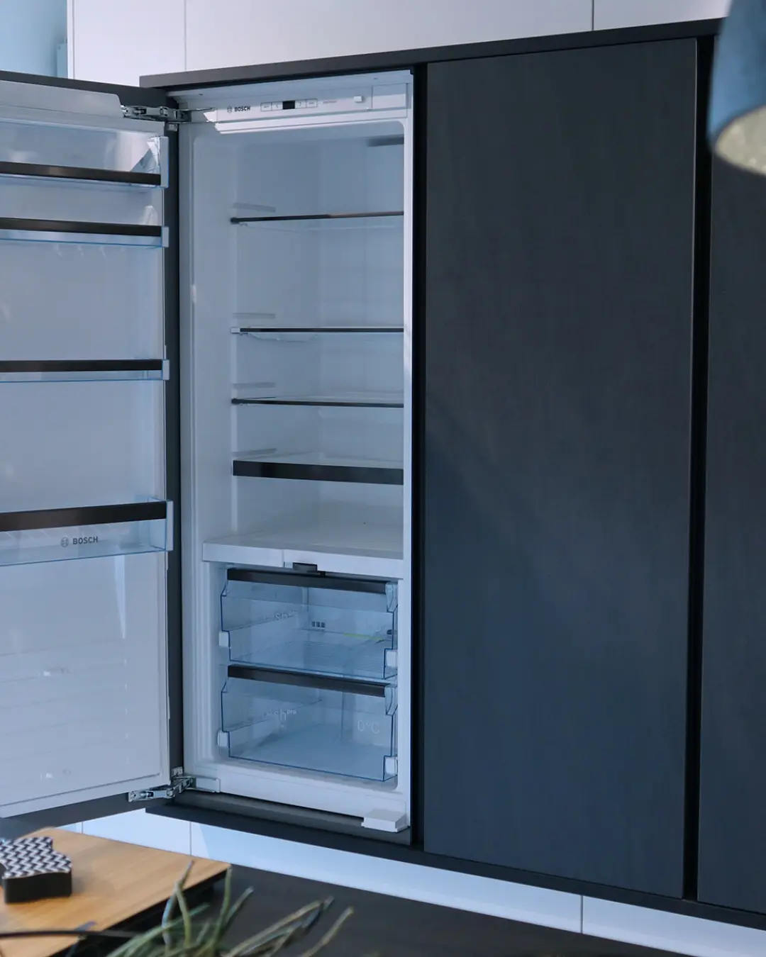Geöffneter Einbaukühlschrank von Bosch in der dunklen Hochschrankfront der Häcker Küche KBK1