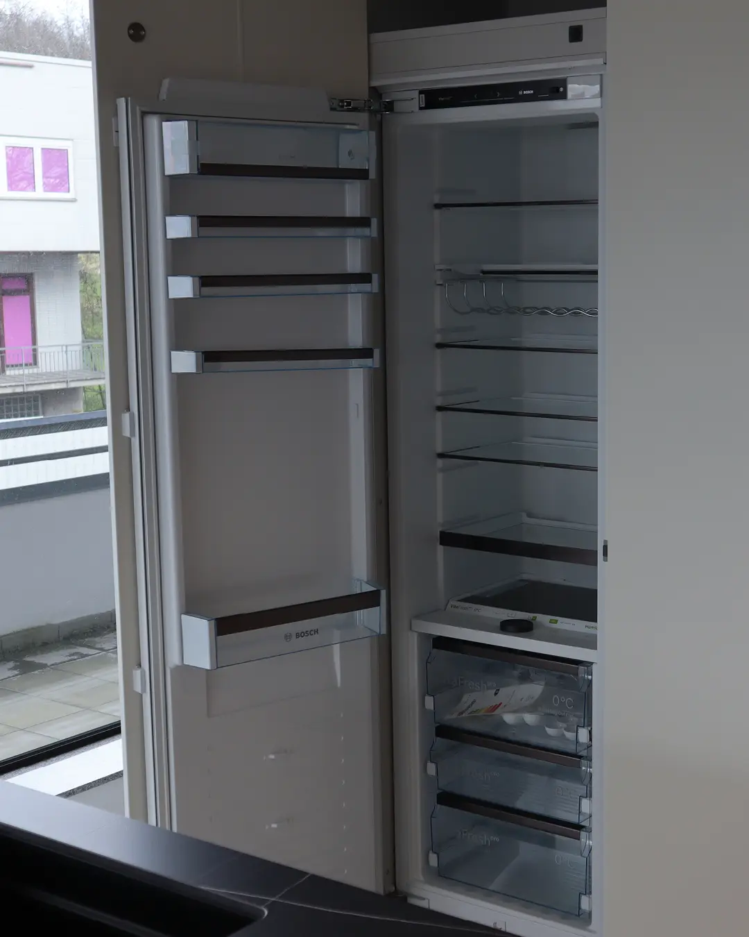 Geöffneter Bosch Einbaukühlschrank mit leeren Ablagen in der weißen grifflosen Leicht Küche KBK21