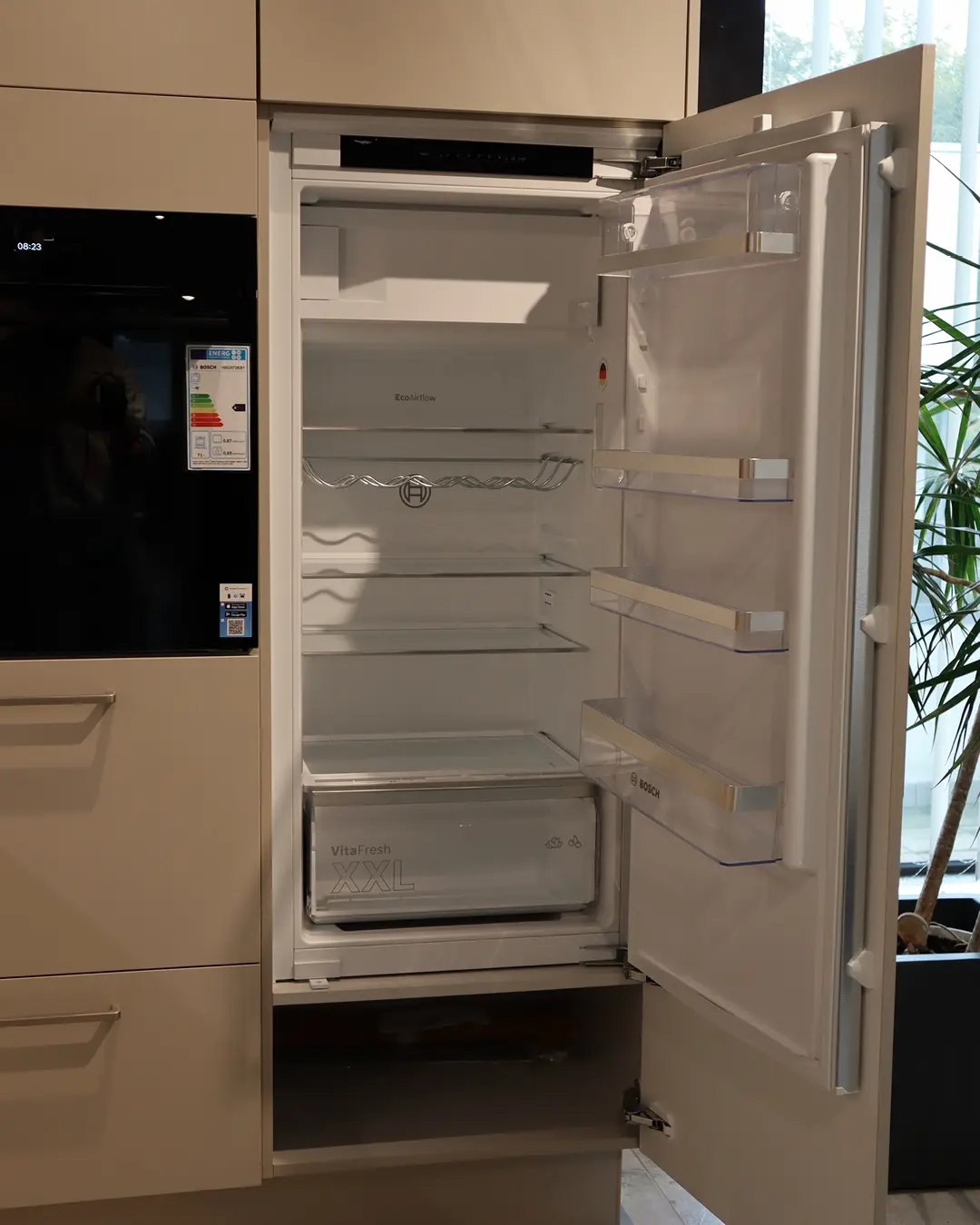 Geöffneter Bosch-Einbaukühlschrank in der Kaschmir Beige Leicht Küche in L-Form, daneben Einbaubackofen