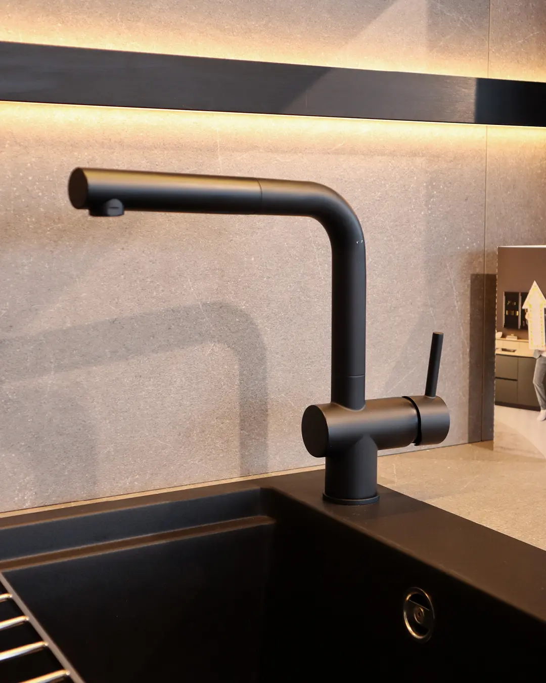 Schwarze Armatur mit Auszugsbrause an schwarzem Spülbecken der grifflosen Nobilia Küche, Rückwand in Steinoptik