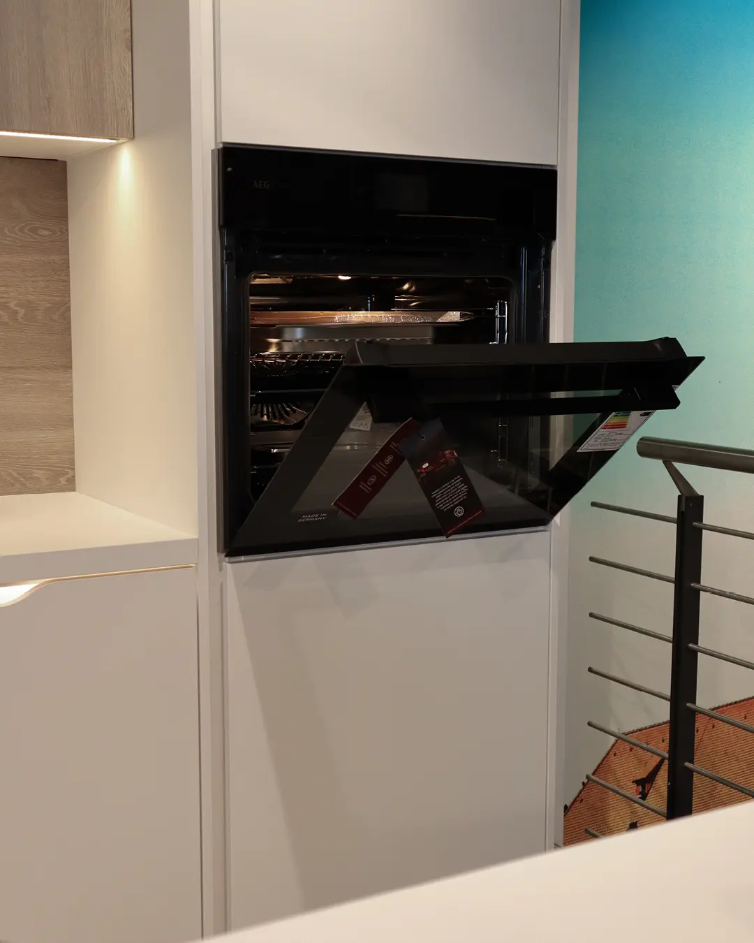 Hochschrank mit geöffnetem Einbaubackofen in einer weißen Nobilia Küche, daneben Fronten in Holzoptik