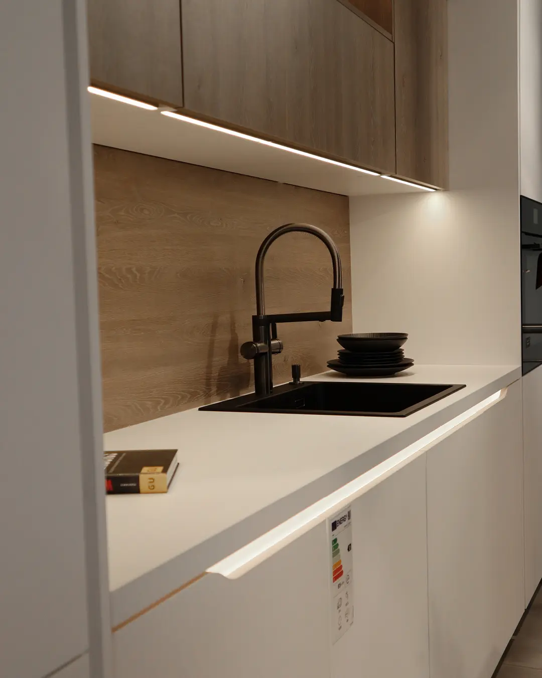 Detail einer Nobilia Küche: weiße Arbeitsplatte mit schwarzer Spüle, Armatur und Rückwand in Holzoptik