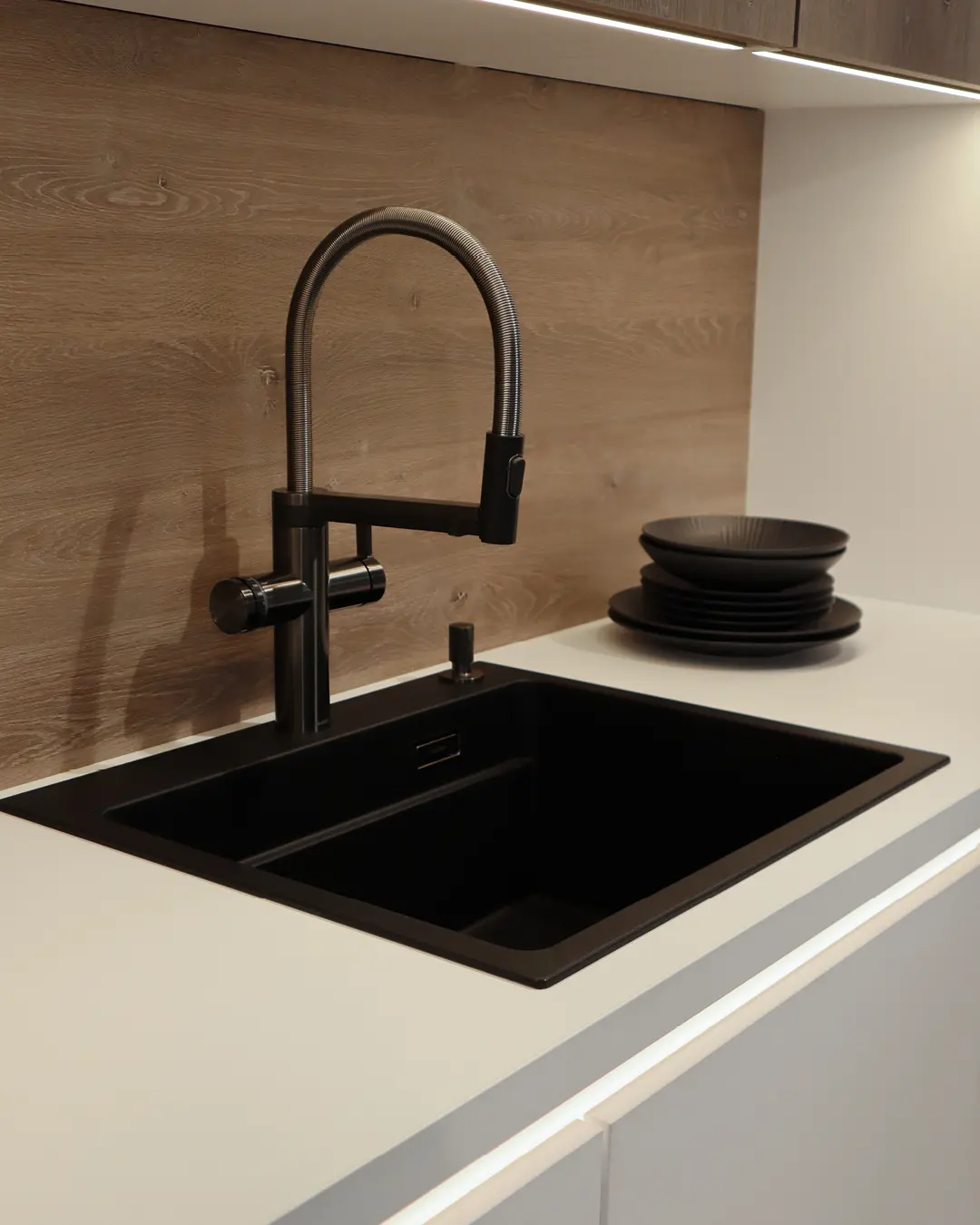 Schwarze Spüle mit schwarzer Profi-Armatur in heller Arbeitsplatte der Nobilia Küche, Rückwand in Holzoptik