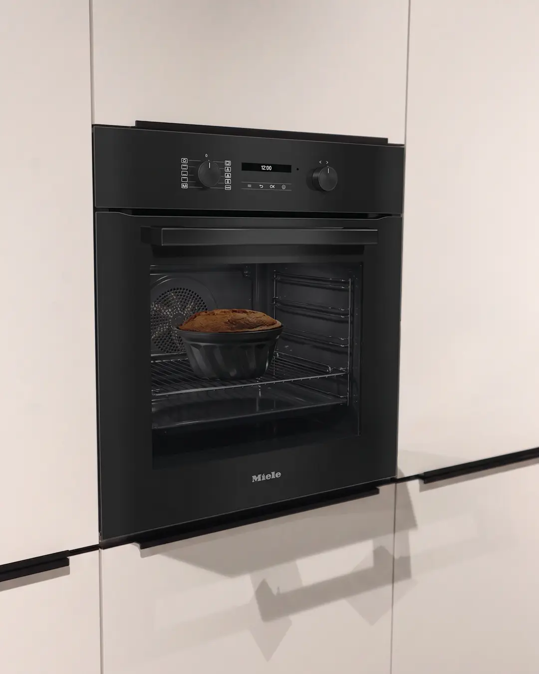 Schwarzer Miele Einbaubackofen mit Kuchen im Inneren in weißer Nobilia Küche in L-Form