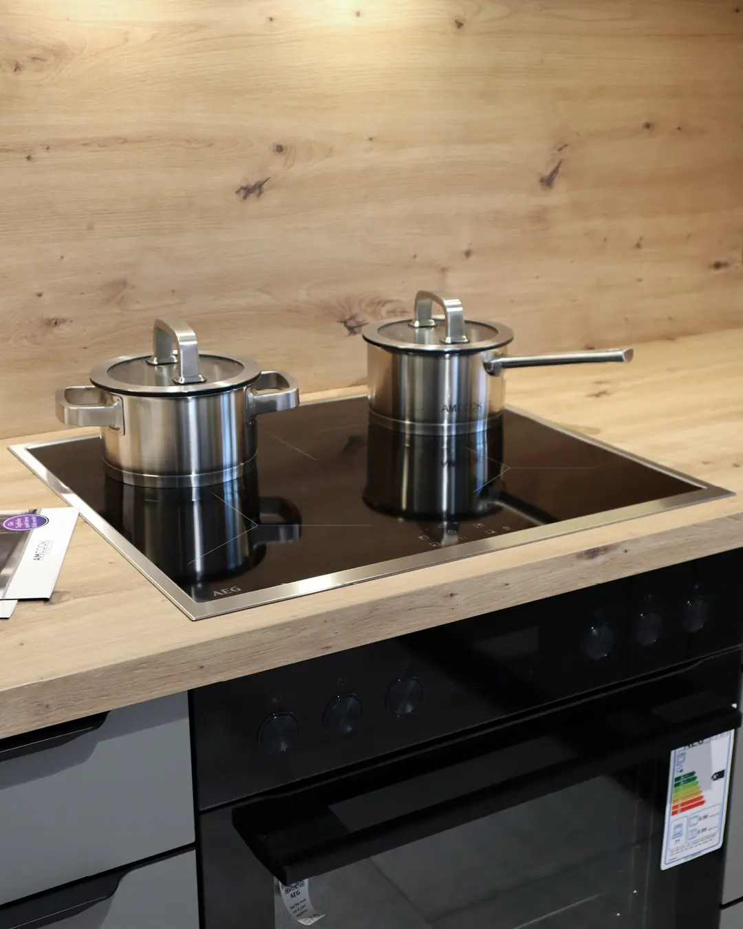 Detail der grauen Nobilia Küche in L-Form: AEG Kochfeld mit zwei Edelstahltöpfen in Arbeitsplatte in Holzoptik