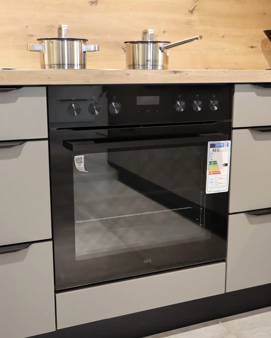 Detail der grauen Nobilia Küche in L-Form: schwarzer AEG Einbaubackofen mit Kochfeld und Arbeitsplatte in Holzoptik