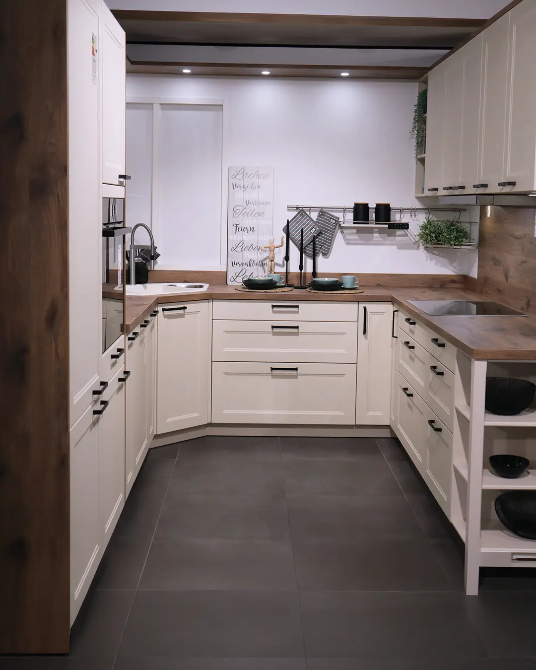 Landhausküche in Crema-Magnolie von Häcker in U-Form mit Arbeitsplatte in Holzoptik und Dekoschild