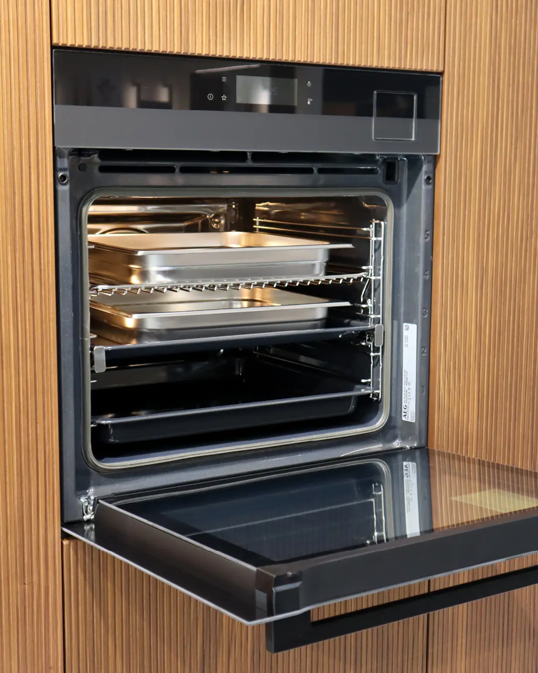 Geöffneter Einbaubackofen mit Blechen in der Häcker Küche KFB10, eingebaut in geriffelte Fronten in Nussbaum-Optik
