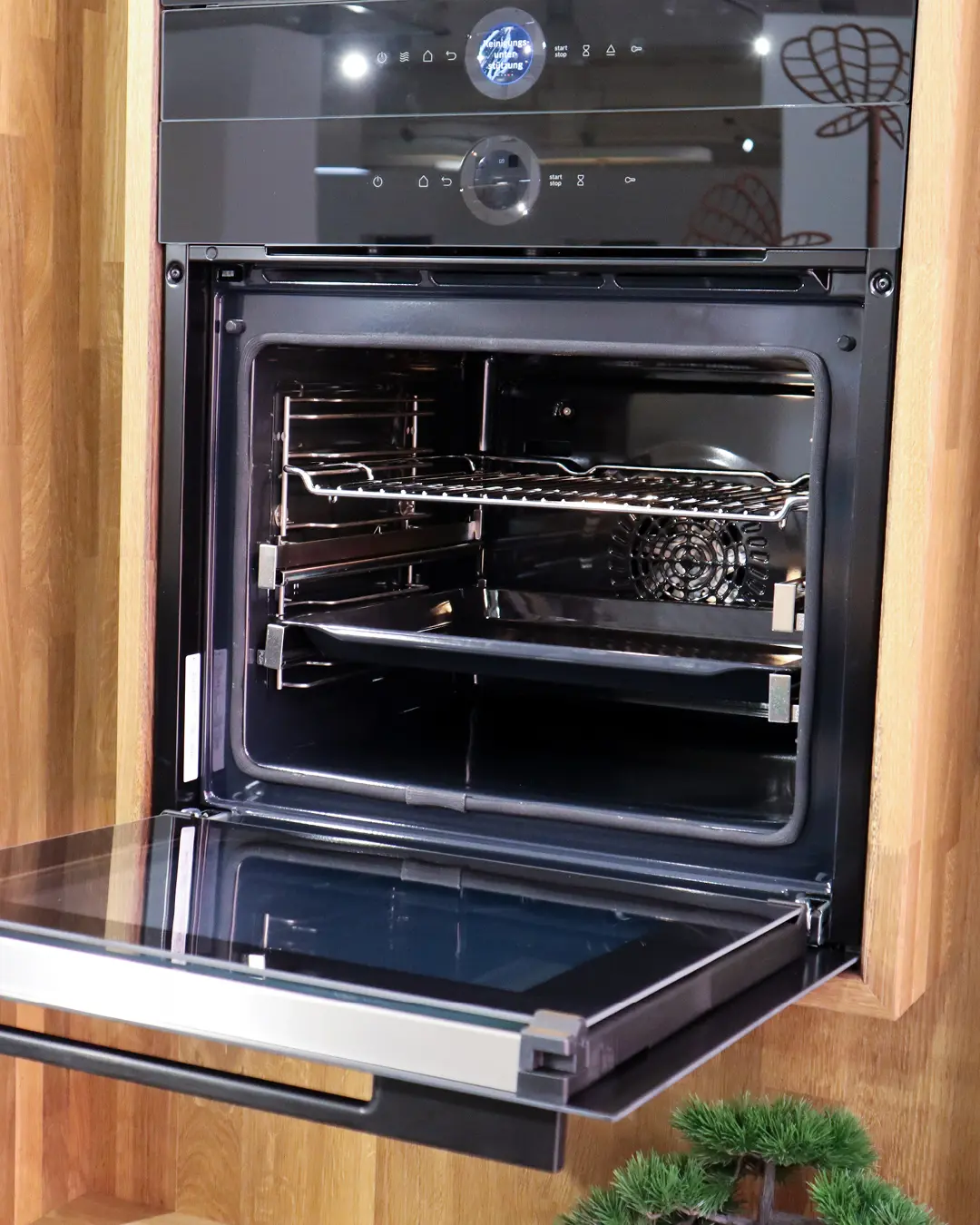 Geöffneter Einbaubackofen mit Rost und Backblech in Hochschrank in Holzoptik der Häcker Küche KFB4