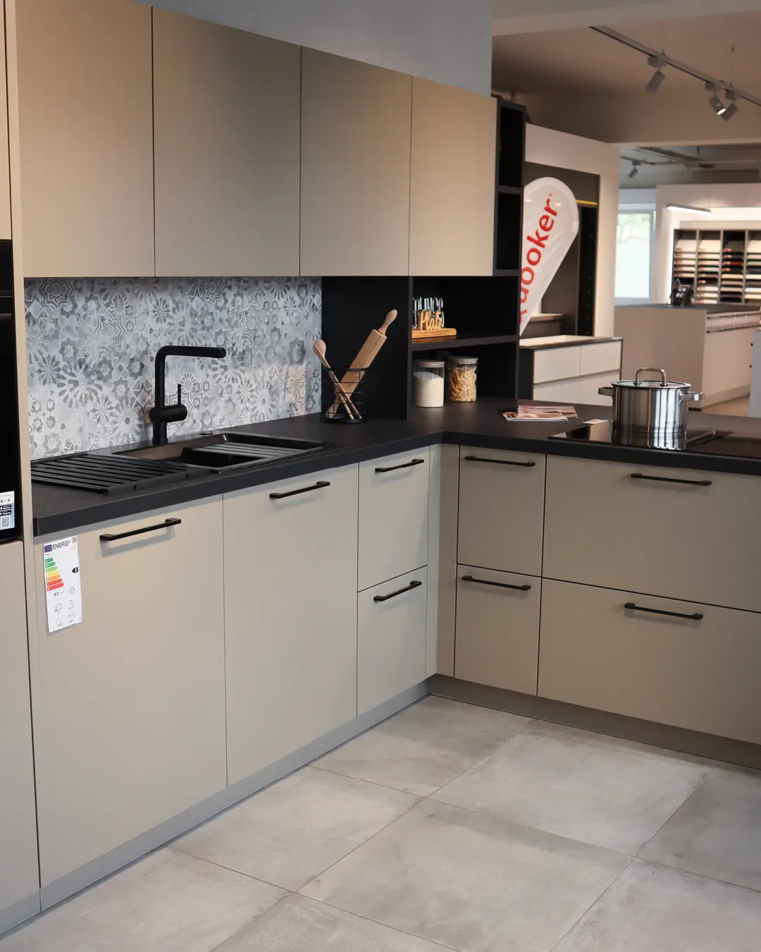 Beige-braune Häcker Küche in L-Form (KBK29) mit dunkler Arbeitsplatte, schwarzer Armatur und gemustertem Fliesenspiegel