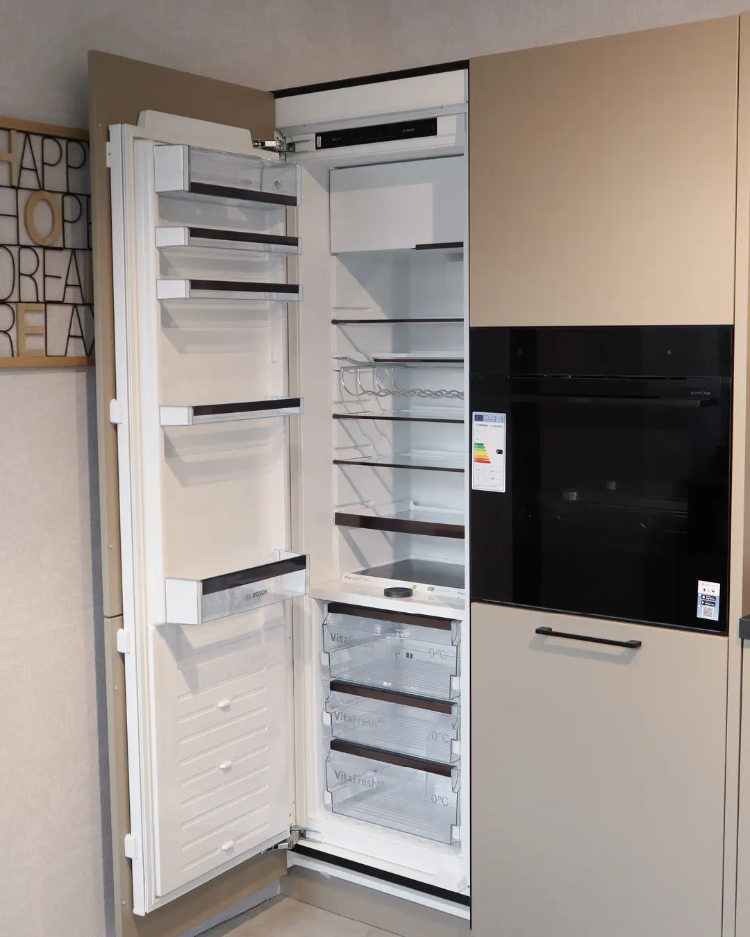 Geöffneter Einbaukühlschrank von Bosch mit Backofen in beiger Häcker Küche in L-Form