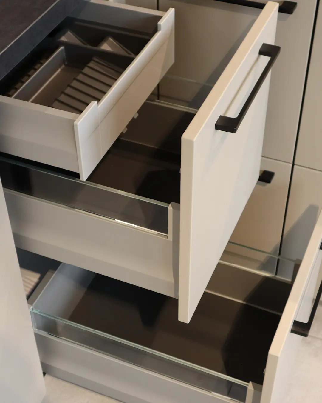 Geöffnete Auszüge mit Glasreling und Besteckeinsatz an einem Unterschrank der beige-braunen Häcker Küche in L-Form