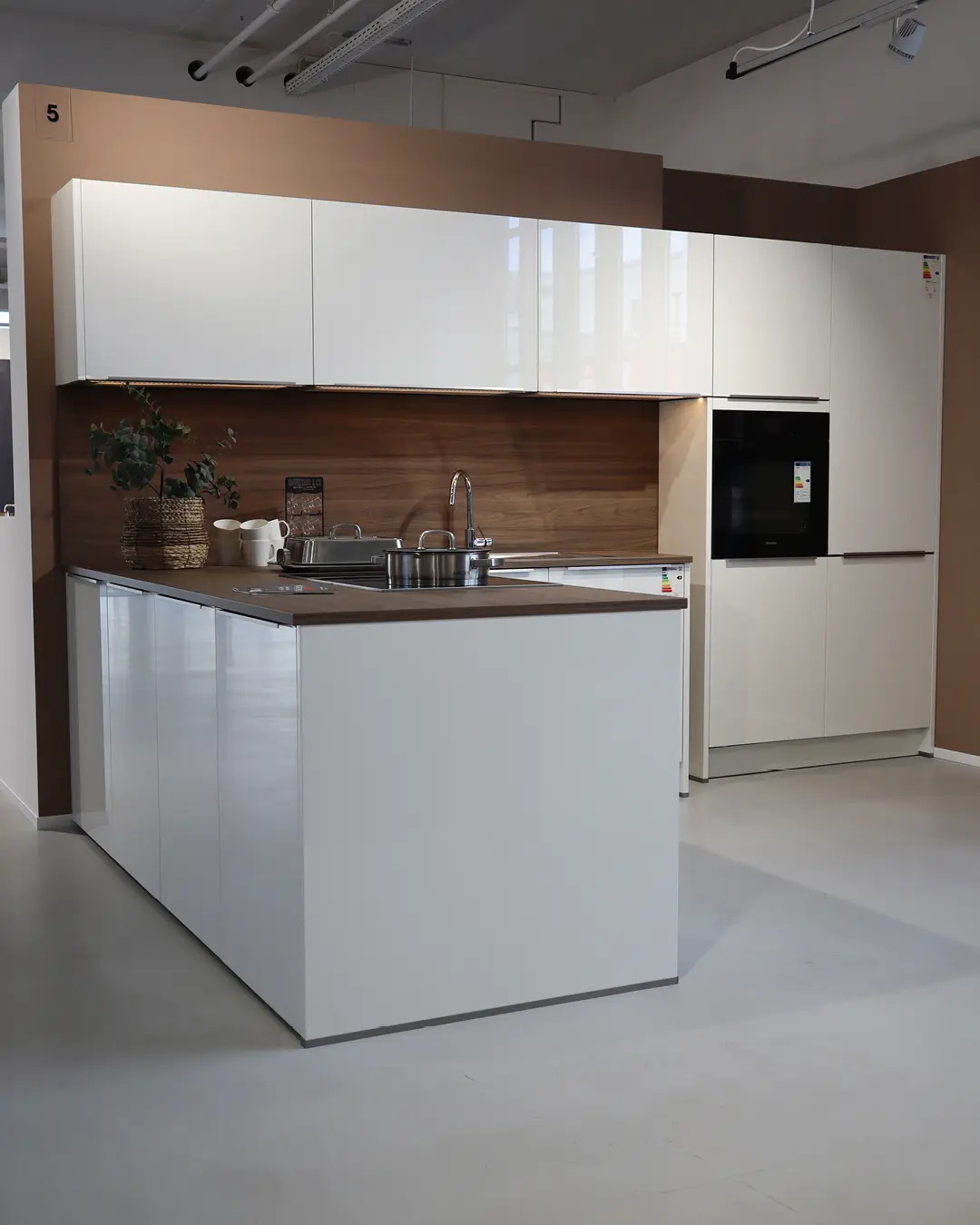 Hochglanz weiße Häcker Küche in L-Form mit Rückwand in Holzoptik, Hochschränken und Backofen