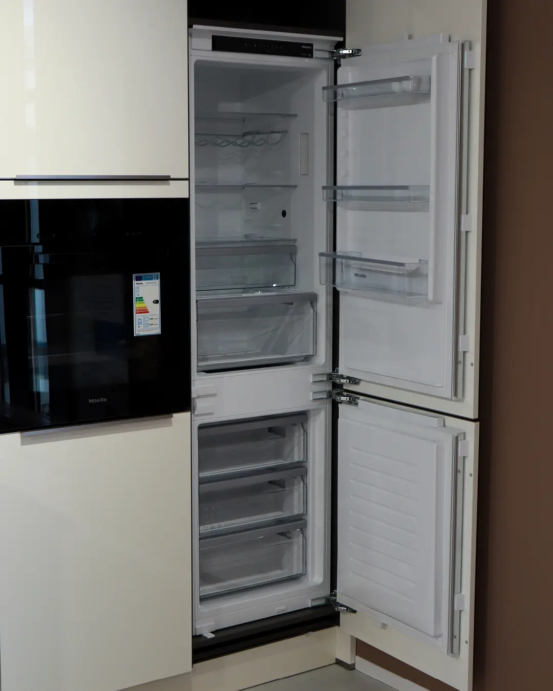 Geöffneter Einbaukühlschrank mit Gefrierfach neben Miele-Backofen in der weißen Häcker Küche KFB5