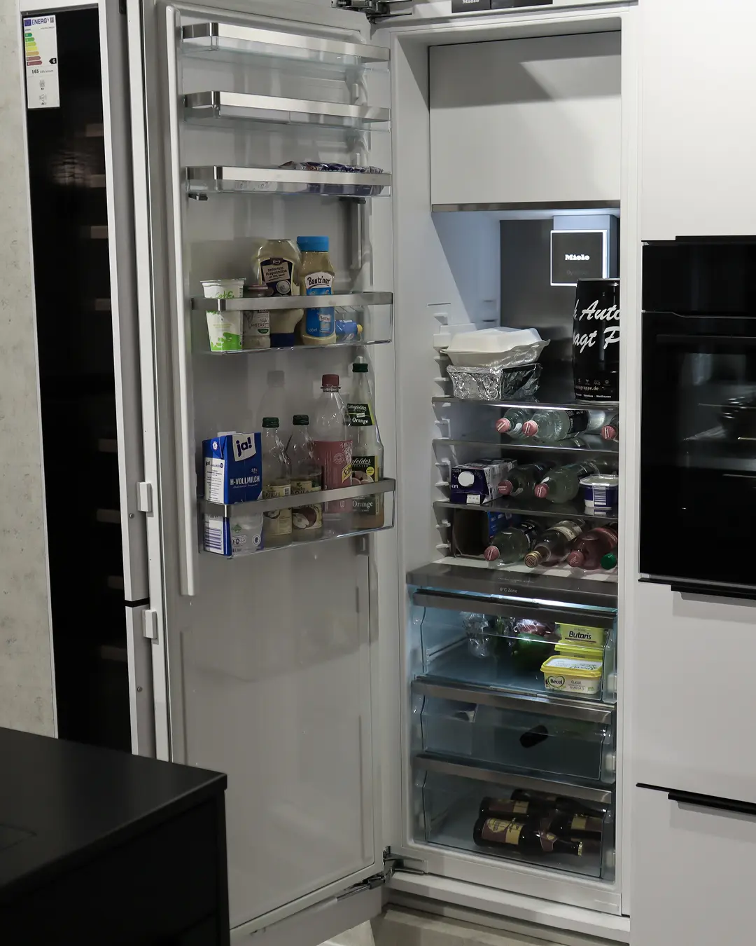 Geöffneter Einbaukühlschrank von Miele mit gefüllten Ablagen in der weißen Häcker Küche KFB6