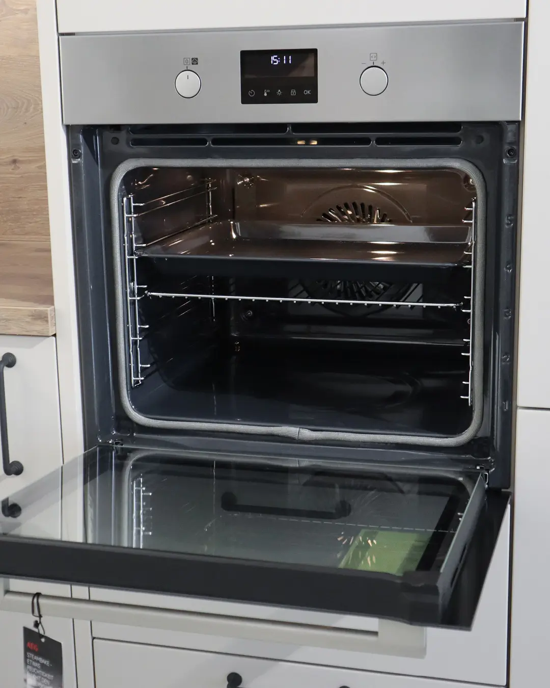 Geöffneter Einbaubackofen mit Edelstahlfront und Displayanzeige in der grauen Landhausküche von Häcker