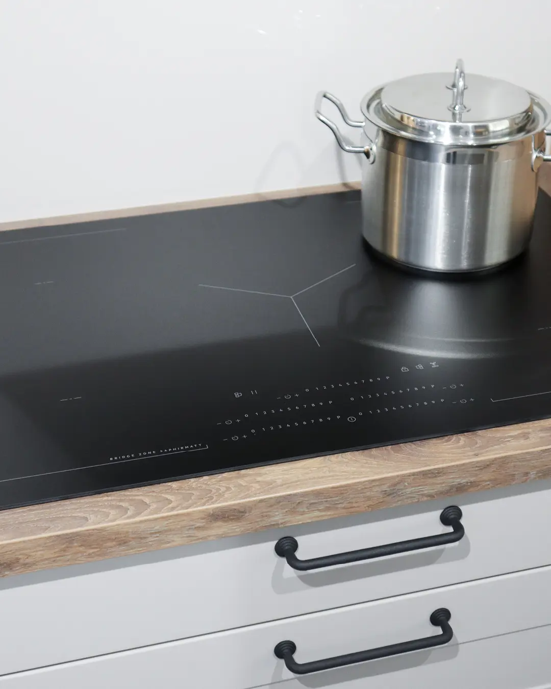 Detail der grauen Landhausküche von Häcker: Induktionskochfeld in Arbeitsplatte in Holzoptik mit Edelstahltopf