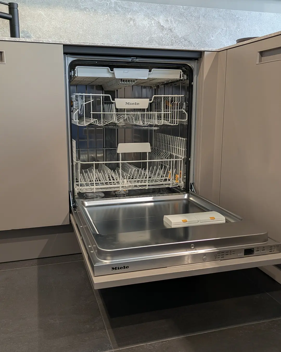 Geöffneter Miele-Geschirrspüler in der sandgrauen Küche von Leicht in U-Form