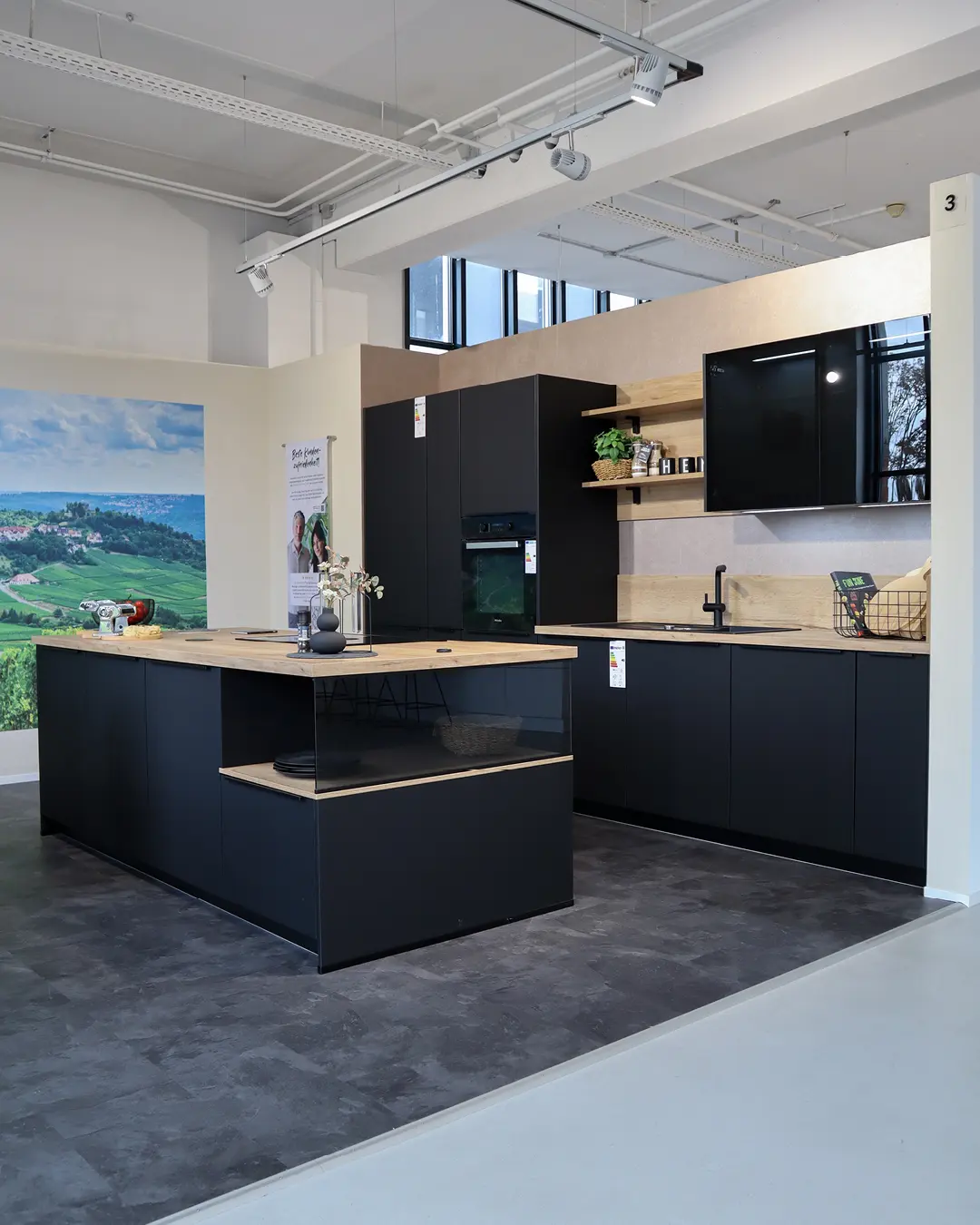 Moderne schwarze Nobilia Küche mit Kochinsel und Arbeitsplatten in Holzoptik in einer Ausstellung