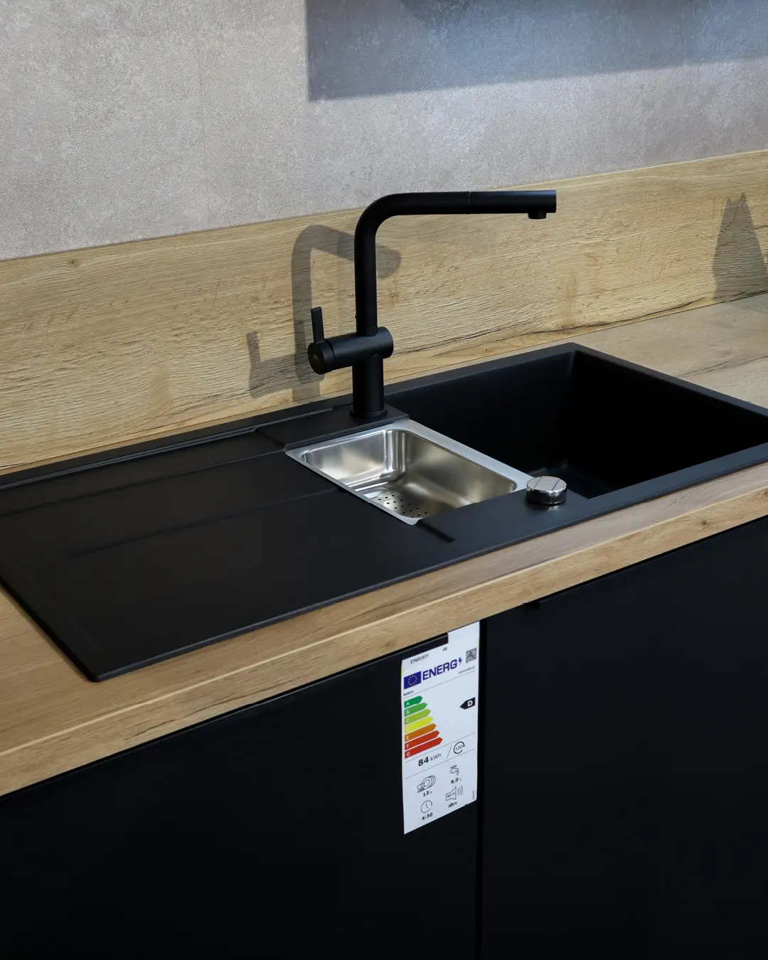 Schwarze Spüle mit schwarzer Armatur in Arbeitsplatte in Holzoptik einer Nobilia Küche mit Kochinsel