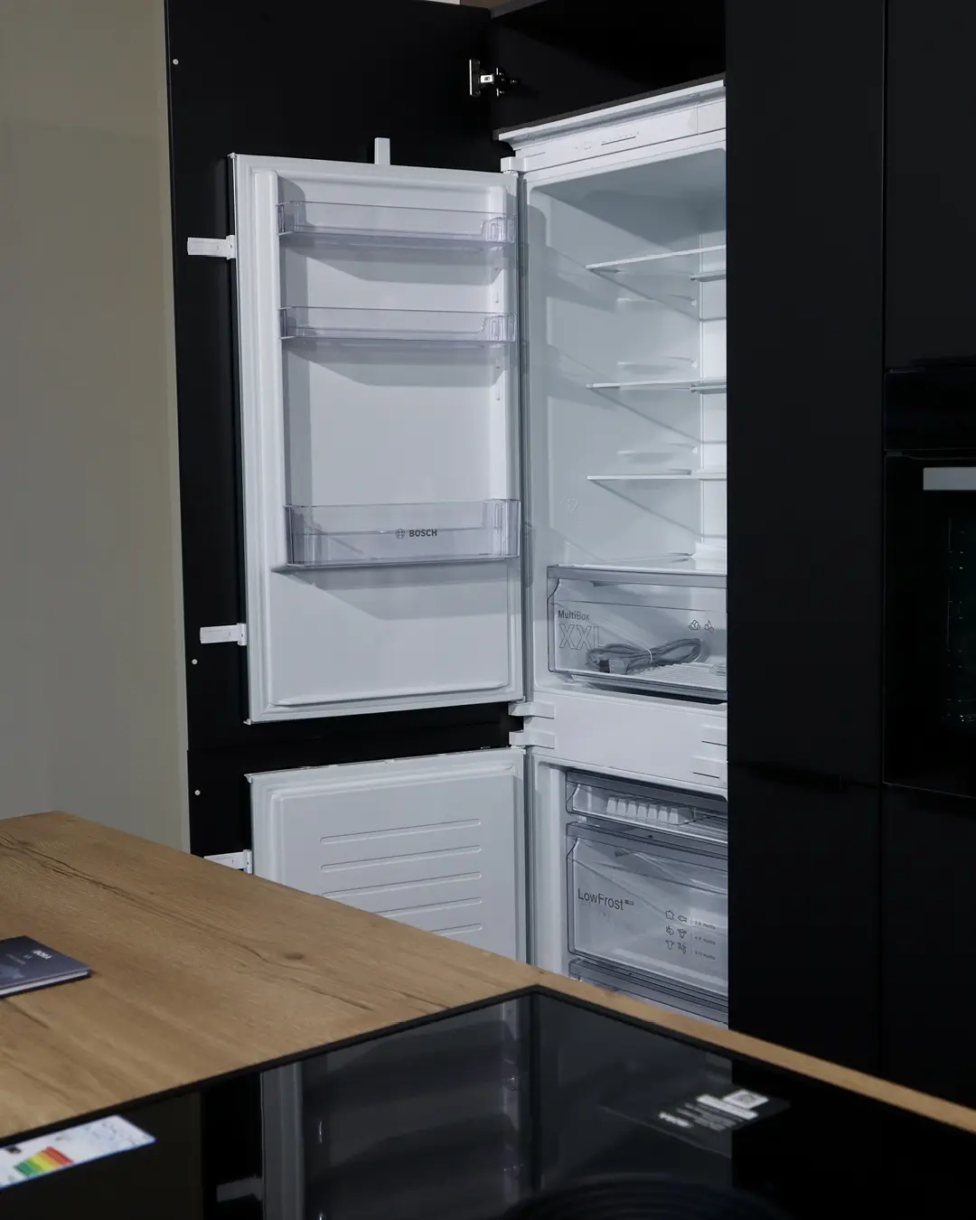 Geöffneter Bosch Einbaukühlschrank in schwarzer Nobilia Küche mit Insel in Holzoptik